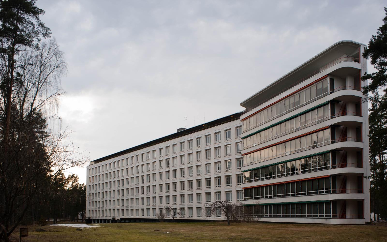 Long white sanatorium building with a curved balcony wing surrounded by trees